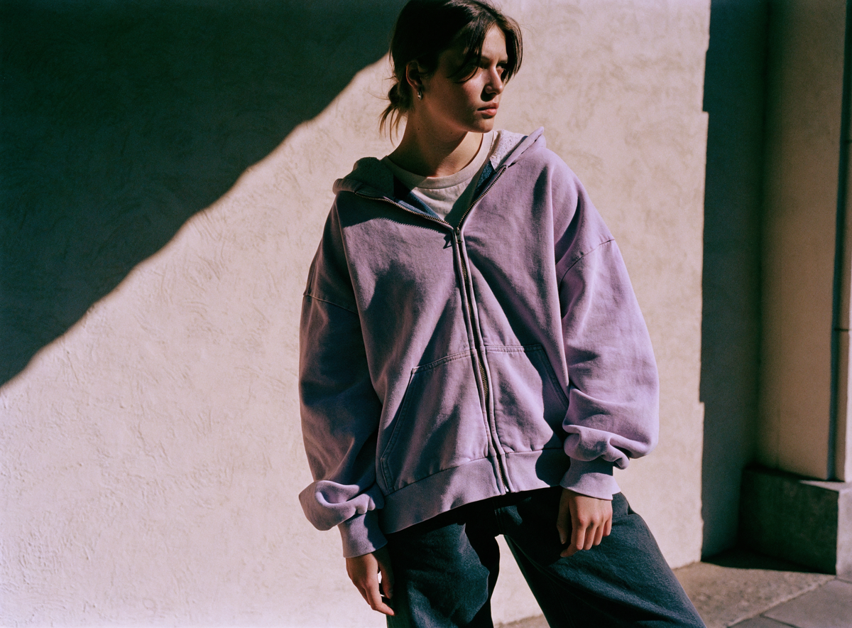 Model wearing a sun-faded pigment-dyed lilac zip hoodie in hard afternoon light