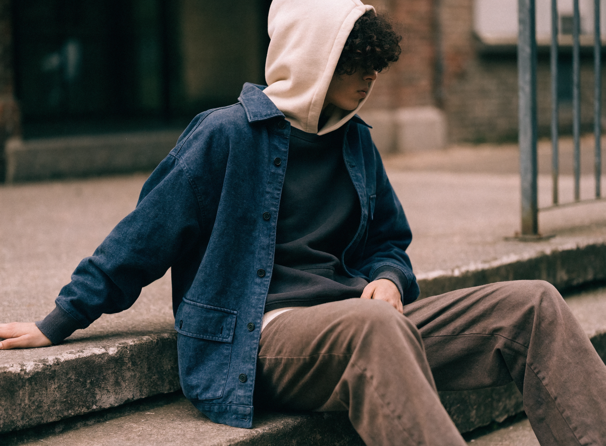 Model wearing a layered capsule outfit of hoodie, crewneck and indigo jacket